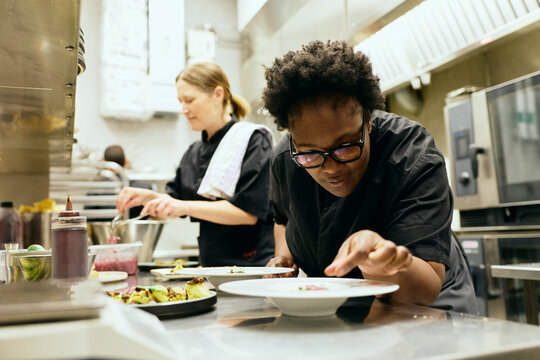 Focused female culinary professional styling food while working inside commercial kitchen