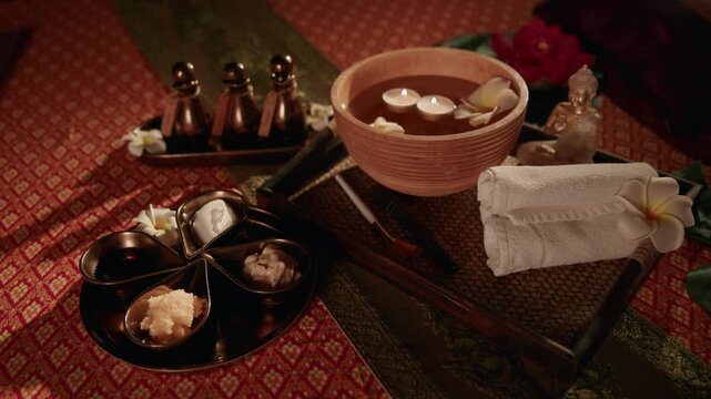 Slow motion spa bowl with floating candles and towel arranged on massage treatment table in wellness room. panning tracking shot.