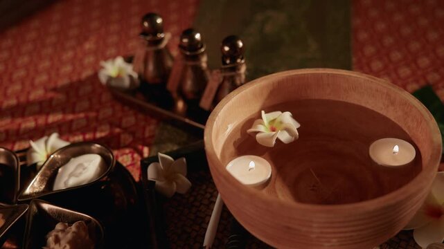 Slow motion closeup of wooden bowl with floating candles and frangipani flowers on spa mat Thai relax.
