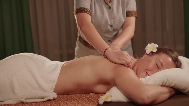 Slow motion woman receiving back massage on spa treatment table in indoor therapy room, Thai aroma relax.