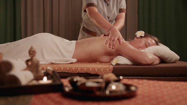 Woman receiving back massage by masseuse on massage table in spa treatment room.