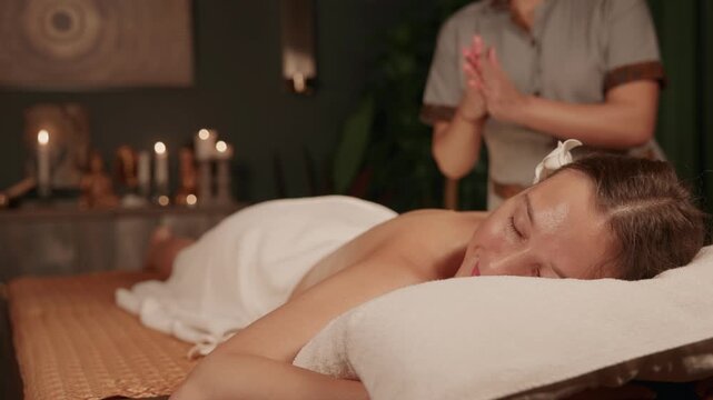 Slow motion woman receiving back massage on spa treatment table in dim candlelit treatment room.