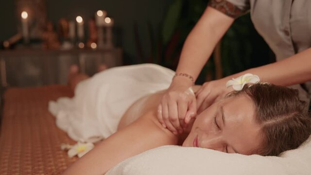 Client caucasian woman receiving back massage on Thai spa treatment table with candlelit ambiance and aroma oil.
