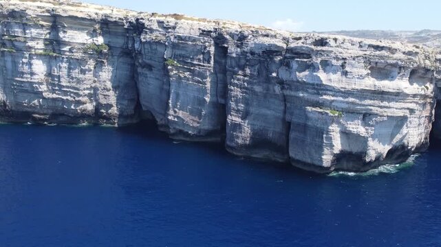 Aerial view of the rugged limestone cliffs and deep blue Mediterranean sea at Dwejra Bay on the coast of Gozo region, Malta. High quality 4k footage
