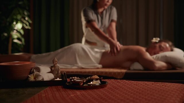 Slow motion therapist massaging woman client on Thailand spa treatment table in dimly lit interior.