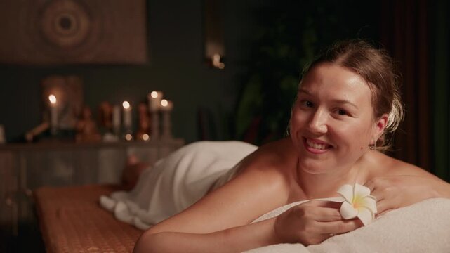 Slow motion portrait young woman receiving massage on spa Thai treatment table in candlelit room.