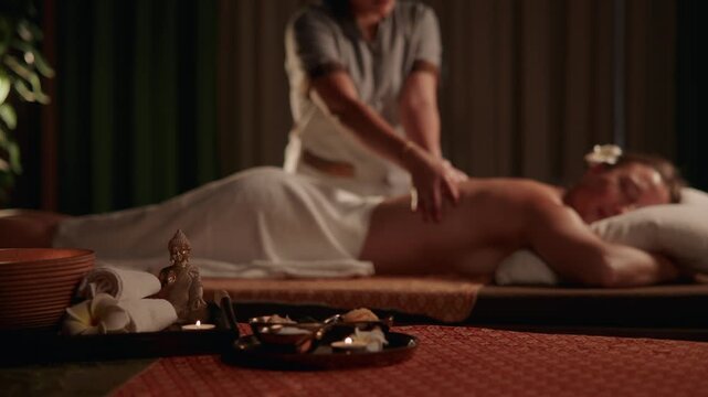 Tracking shot of therapist massaging woman on massage table in candlelit spa treatment room with slow smooth pan.