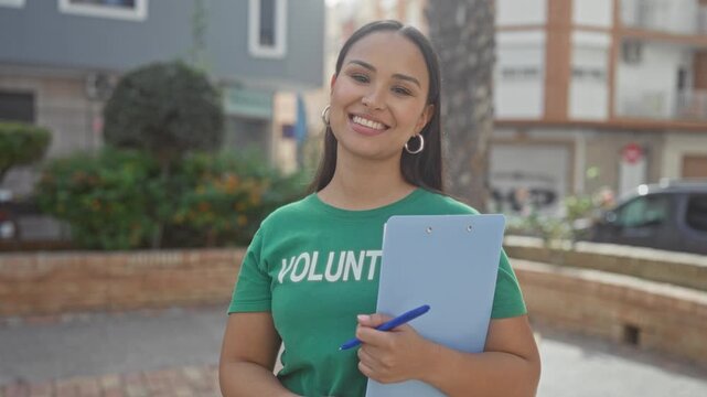 Woman holding clipboard and pen with visible hand, smiling in volunteer tshirt on a street; friendly community service.