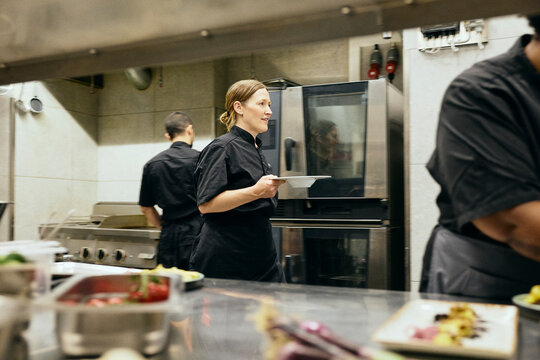 Busy female chef holding plate while walking in kitchen during service