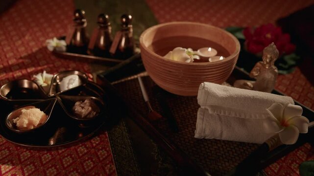 Slow motion spa bowl and towel arrangement on woven massage table in thai wellness treatment setting. static shot.