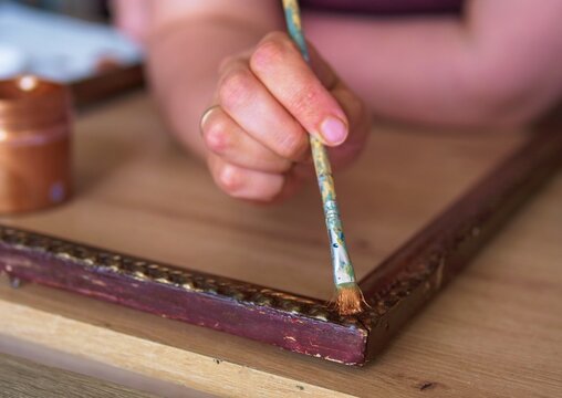 Close-up of Hand Restoring a Vintage Wooden Picture Frame with Gold Paint