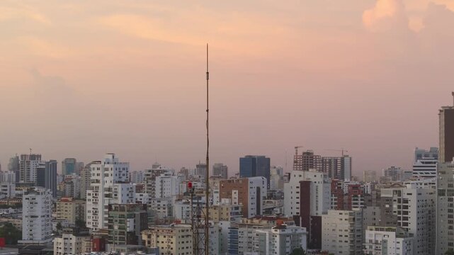 Dense city skyline view featuring a tall radio antenna spire against a warm sunset sky