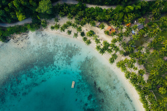 Aerial view of Port Barton beach with lush palm trees, turquoise water, and a small wooden boat, San Vicente, Mimaropa, Philippines.