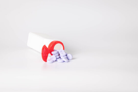 Large, round purple chewable tablets spilling out of a white bottle with red lid onto a white background.