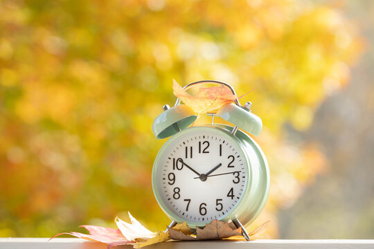 Autumn time change concept.  Fall Back 1 Hour or time is running out.  Alarm clock with sunlit colorful fall foliage in background