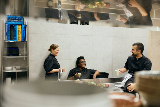 Three professional restaurant chefs laughing and drinking coffee during break time