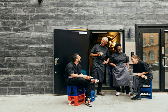 Happy male and female chefs enjoying during their break time while sitting by back door