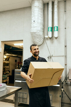 Professional male chef carrying food supply box in commercial kitchen
