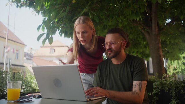 Creative freelance couple resolving project conflict on laptop in outdoor coffee shop