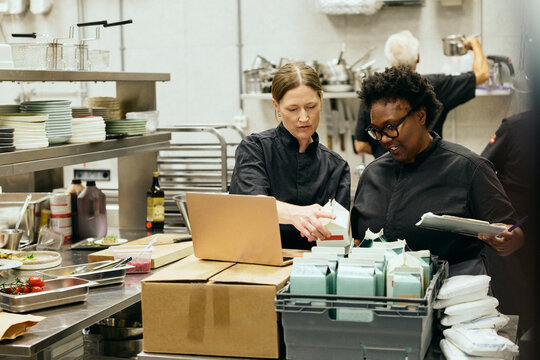 Restaurant chefs checking inventory on laptop in while working in kitchen