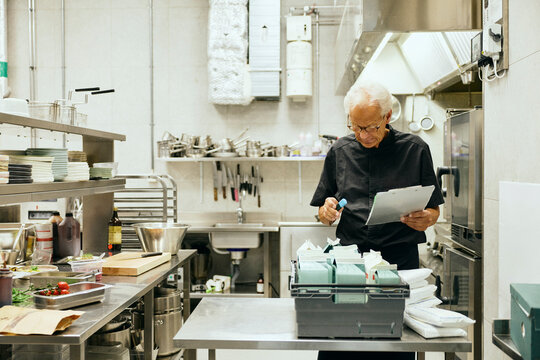 Senior male chef taking stock inventory in restaurant kitchen