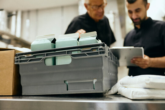 Two chefs in black uniforms inspecting incoming stock packages arranged in crate
