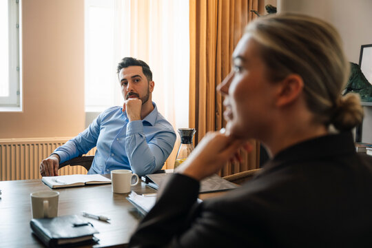 Businessman with hand on chin looking at his female colleague while sitting in office meeting