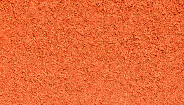 Close-up view of a vibrant orange stucco wall surface featuring a grainy, coarse, and rough texture that creates a dynamic play of light and shadows across the painted plaster facade