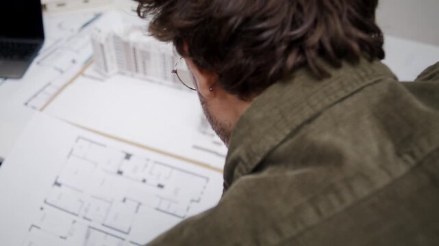 Architect in glasses studies detailed sketch of modern building