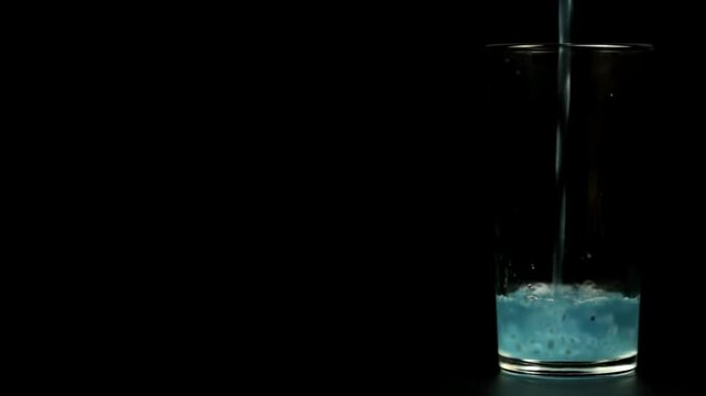 A healthy turquoise drink with seeds is poured into a transparent glass