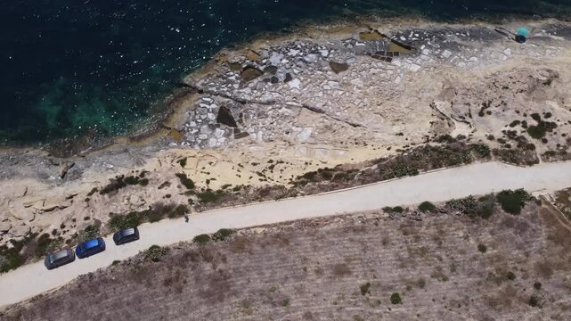 Xatt L-Ahmar, salt pans, Gozo island, Malta. serene aerial view of rocky coastline with clear blue ocean waves and sandy shorelines during a peaceful vacation in nature. High quality 4k footage