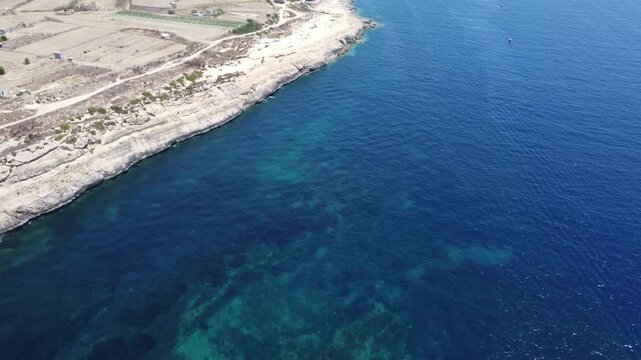 serene aerial view of a tranquil coastline of Gozo, Xatt L-Ahmar, near salt pans with blue ocean and green land under a bright sky. High quality 4k footage