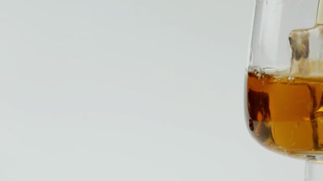 Cognac is poured into a glass with ice on a white background