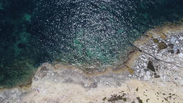 Xatt L-Ahmar, salt pans, Gozo island, Malta. serene aerial view of rocky coastline with clear blue ocean waves and sandy shorelines during a peaceful vacation in nature. High quality 4k footage