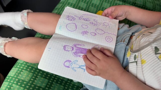Child's hands holding an open notebook with colorful drawings on a grid paper