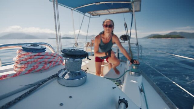 Couple sailing the small sailing boat in the calm sea during nice sunny day, man steers and woman works with the ropes