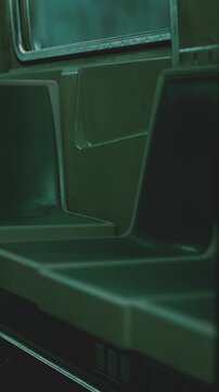 The view shows empty seats inside a subway train. The lighting is dim and creates shadows. The train appears to be idle on a quiet route at night.