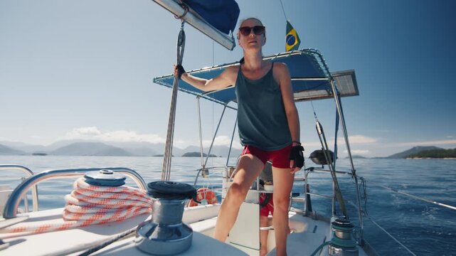 Couple sailing the small sailing boat in the calm sea during nice sunny day, man steers and woman works with the ropes