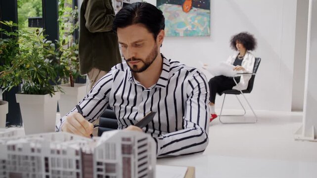 Man architect attentively observes miniature apartment buildings