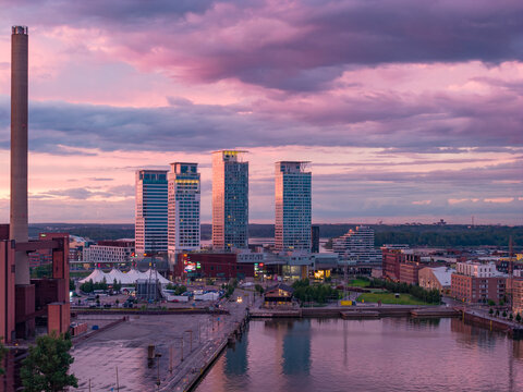 Aerial view of the Hanasaari power plant area with modern high-rise buildings, waterfront docks, and a dramatic purple sunset sky over Helsinki, Uusimaa, Finland.
