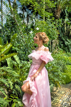 Elegant woman in luxury pink dress posing in tropical botanical garden greenhouse