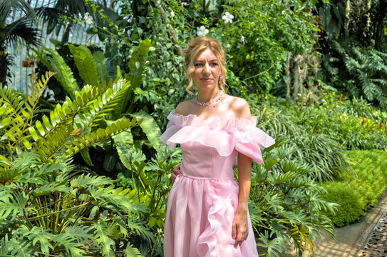 Beautiful sensual woman in elegant pink gown looking away in tropical glasshouse