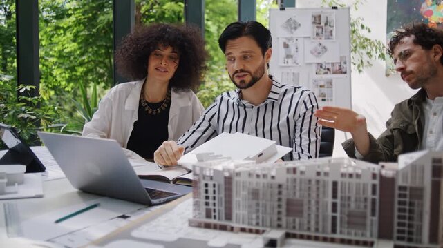 Multicultural designers plan urban district on laptop in office