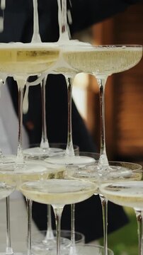 Vertical video. Close-up of champagne glass pyramid with blurred bride and groom in the background.