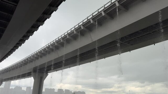 Rain pours from the gutters of the road bridge.