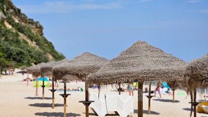 Fototapeta premium Straw beach umbrellas on sunny coast, summer resort vacation background