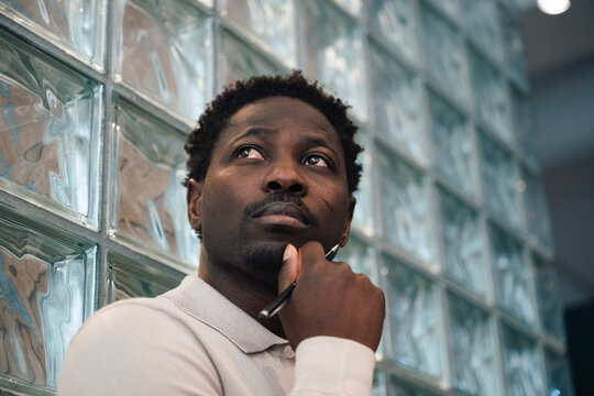 Low angle view of thoughtful businessman with hand on chin by glass brick wall