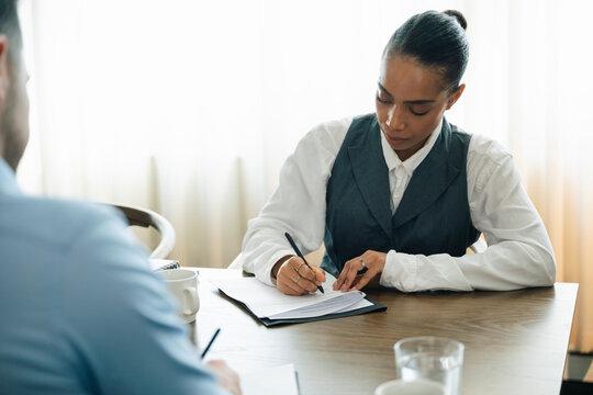 Businesswoman completing paperwork for client while sitting in office meeting room