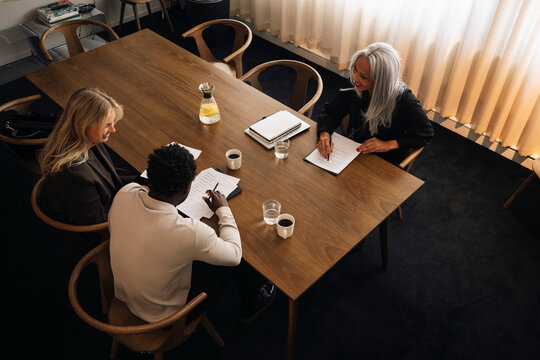 High angle view of diverse team reviewing documents with coffee in corporate boardroom