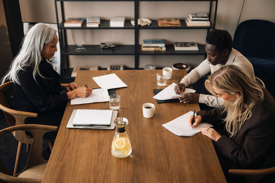 High angle view of diverse couple signing legal separation documents at wooden table